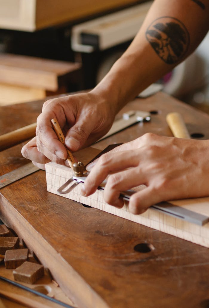 pexels-photo-5974396 From above of crop unrecognizable tattooed male carpenter measuring wooden plank while creating new object in workshop